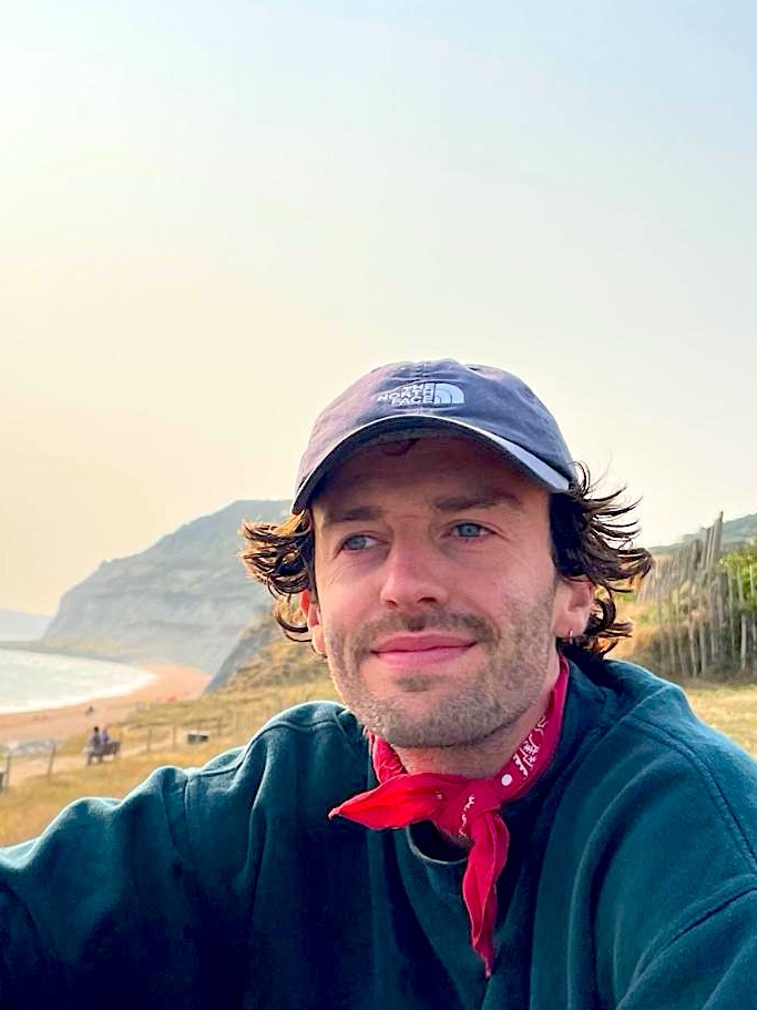 George in a cap and red bandana on a clifftop above the sea